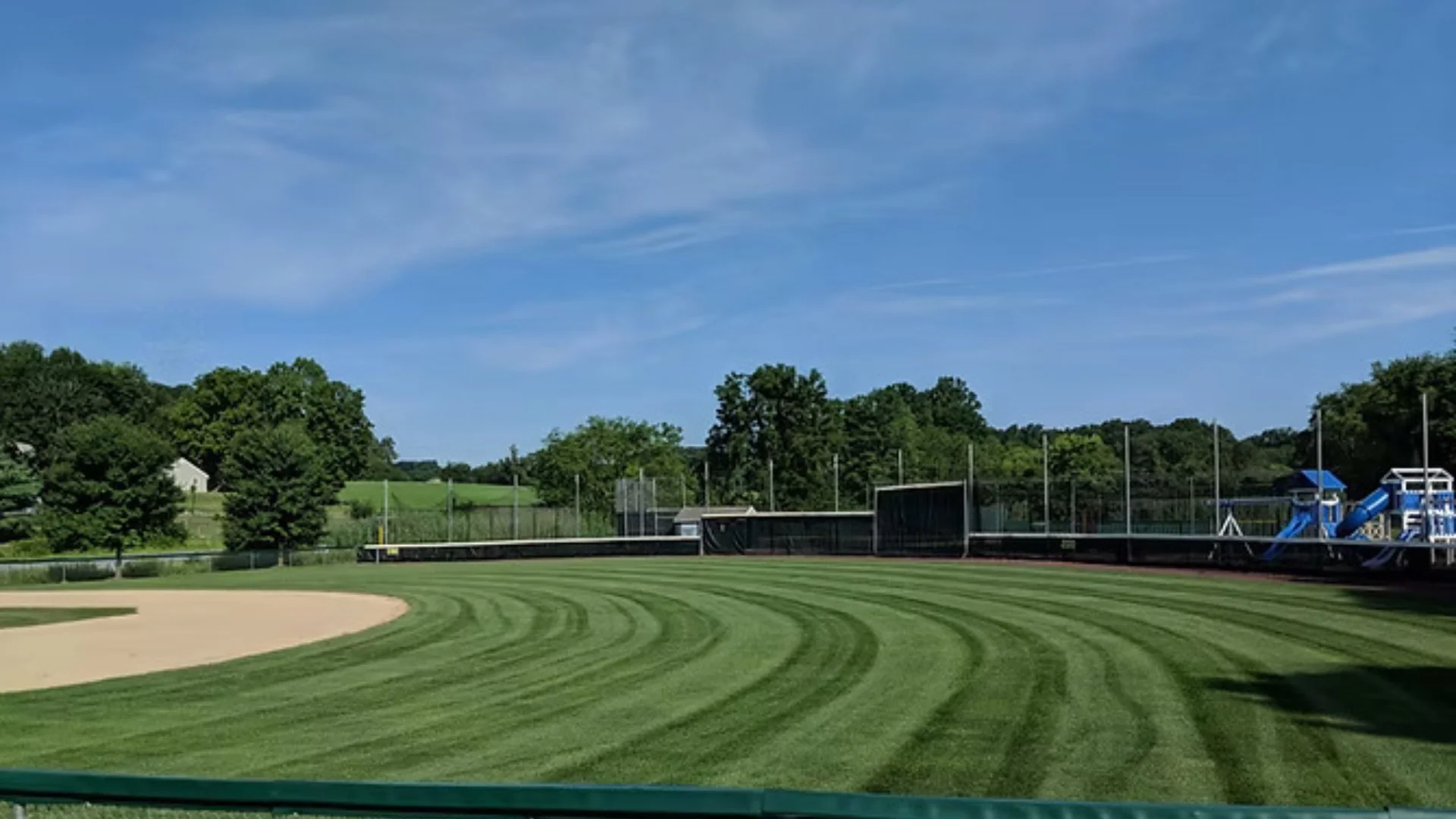Expansive baseball field with manicured grass and a picturesque landscape, featuring a playground in the background, in Doylestown, PA.